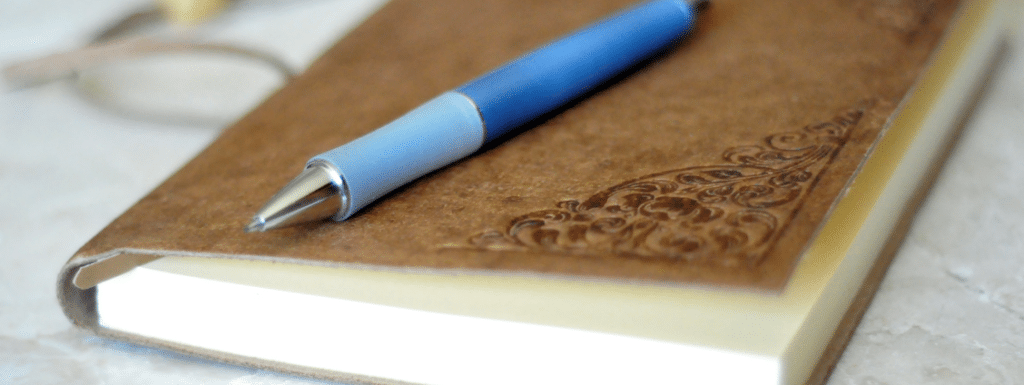 A close picture of a brown journal cover and blue pen on top.