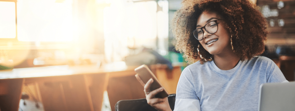 A person of color looking and smiling at a phone.  