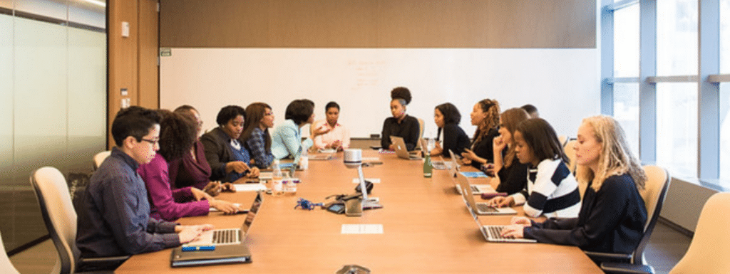 A large group of people with laptops sat at an oval conference table.
