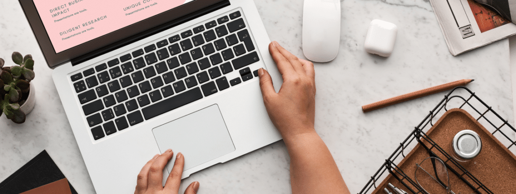 A top view of a desk with person's hands on a laptop and different items on the desk. 