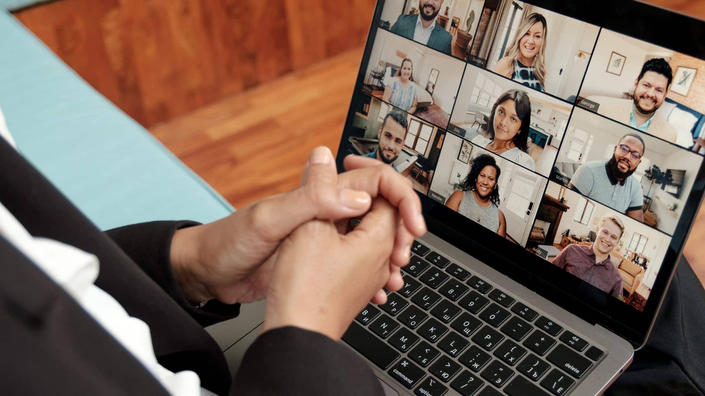 Person sitting with hands clasped, viewing a video call with multiple participants on a laptop screen.