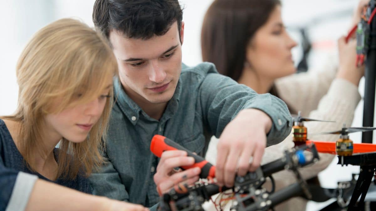 Feature image: Students working together to assemble a drone, with one using a screwdriver on the frame while others assist in the background.