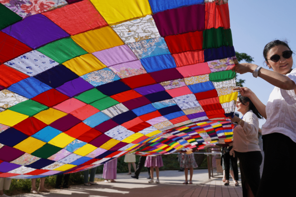 feature image: A colorful patchwork fabric canopy made of mixed-fabric squares stretches overhead outdoors, held up by a person in sunglasses and a white blouse in the foreground.
