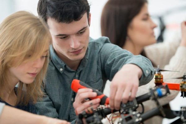 Feature image: Students working together to assemble a drone, with one using a screwdriver on the frame while others assist in the background.