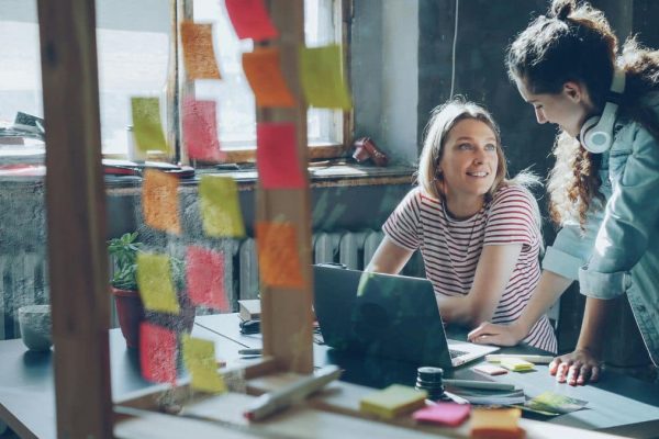 Feature image: two colleagues collaborate at a desk in a sunlit studio