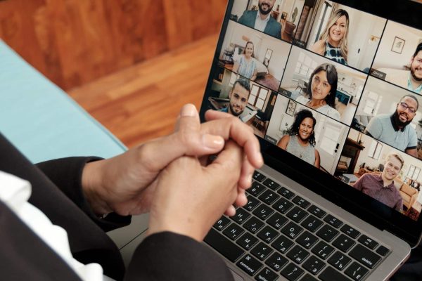 Person sitting with hands clasped, viewing a video call with multiple participants on a laptop screen.